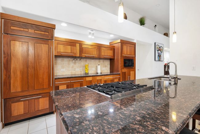 Kitchen with a sink, brown cabinets, built in appliances, decorative light fixtures, and backsplash | Image 7