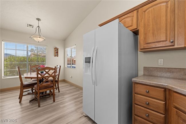 Kitchen with white fridge with ice dispenser, vaulted ceiling, light wood-type flooring, brown cabinetry, and decorative light fixtures | Image 16