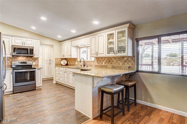 Kitchen with appliances with stainless steel finishes, a breakfast bar area, light stone countertops, vaulted ceiling, and decorative backsplash | Image 21