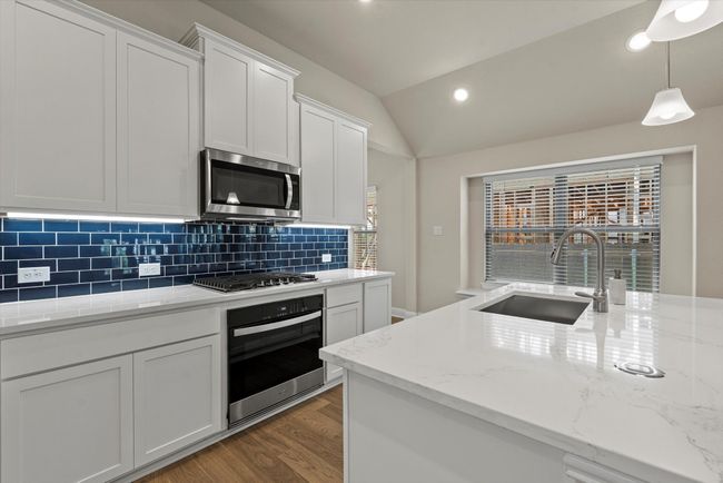 Kitchen with wall oven, stainless steel microwave, a sink, wood finished floors, and backsplash. | Image 7