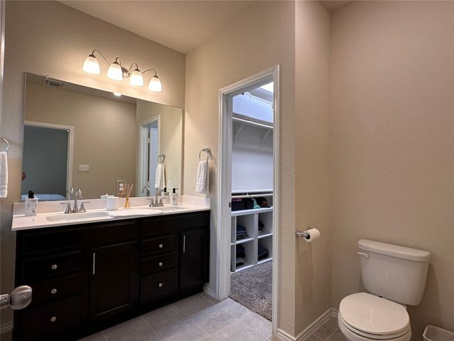 Bathroom featuring toilet, tile patterned floors, double vanity, a walk in closet, and baseboards | Image 32