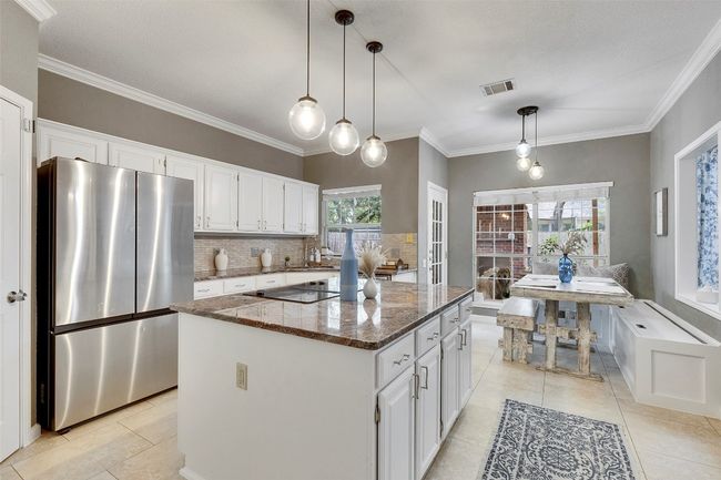 Kitchen featuring freestanding refrigerator, black electric stovetop, white cabinets, dark stone counters, and a center island | Image 9