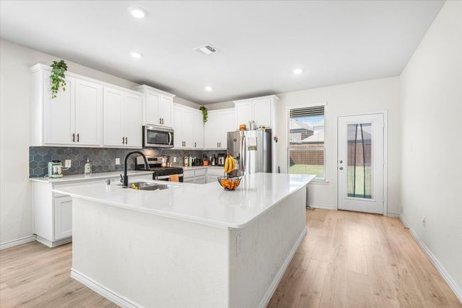 Kitchen featuring light wood-style flooring, appliances with stainless steel finishes, light countertops, and backsplash | Image 9