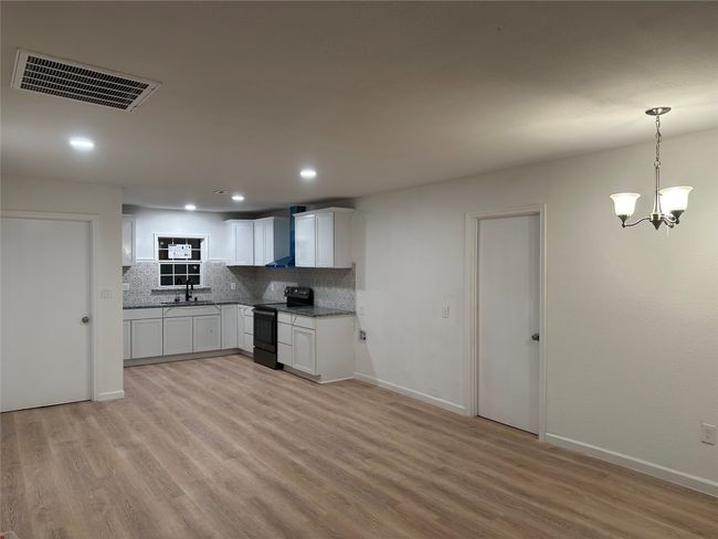 Kitchen with light wood-style floors, visible vents, decorative backsplash, and black electric range oven | Image 5