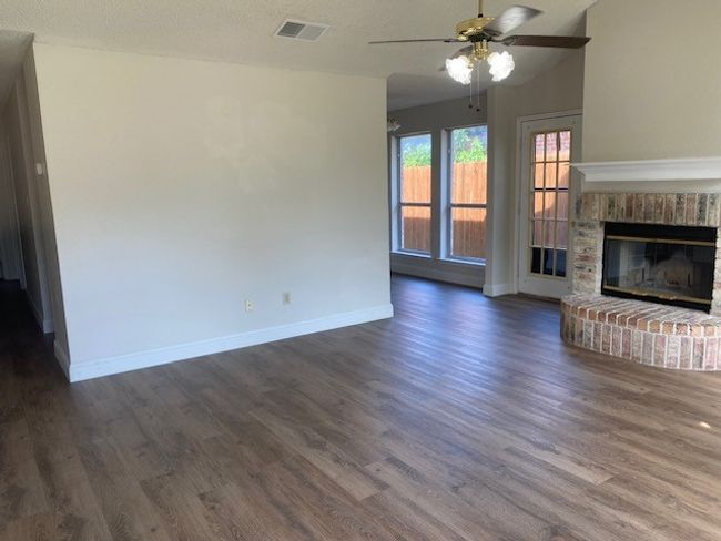 Unfurnished living room with dark wood finished floors, ceiling fan, and a fireplace | Image 4