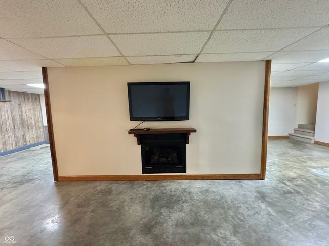 finished basement with a paneled ceiling, baseboards, stairs, wooden walls, and a fireplace | Image 66