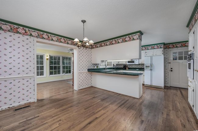 Kitchen with kitchen peninsula, decorative light fixtures, white cabinets, white appliances, and dark hardwood / wood-style floors | Image 13