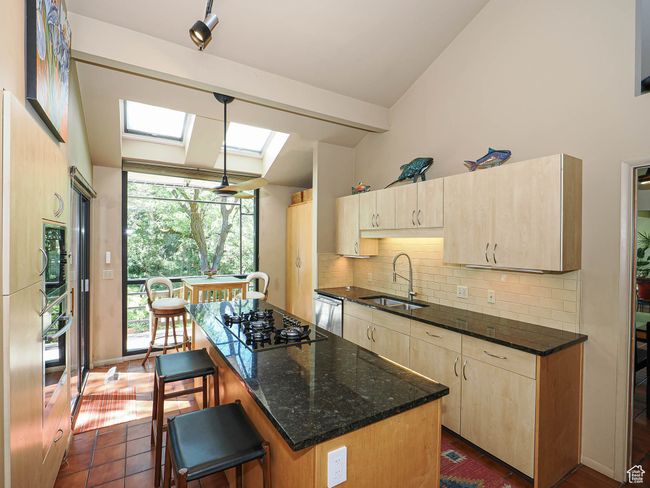 Kitchen featuring black gas cooktop, lofted ceiling, a skylight, light brown cabinets, and backsplash | Image 21