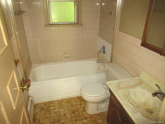 Bathroom featuring a baseboard heating unit, tile walls, vanity, and shower / tub combination | Image 10