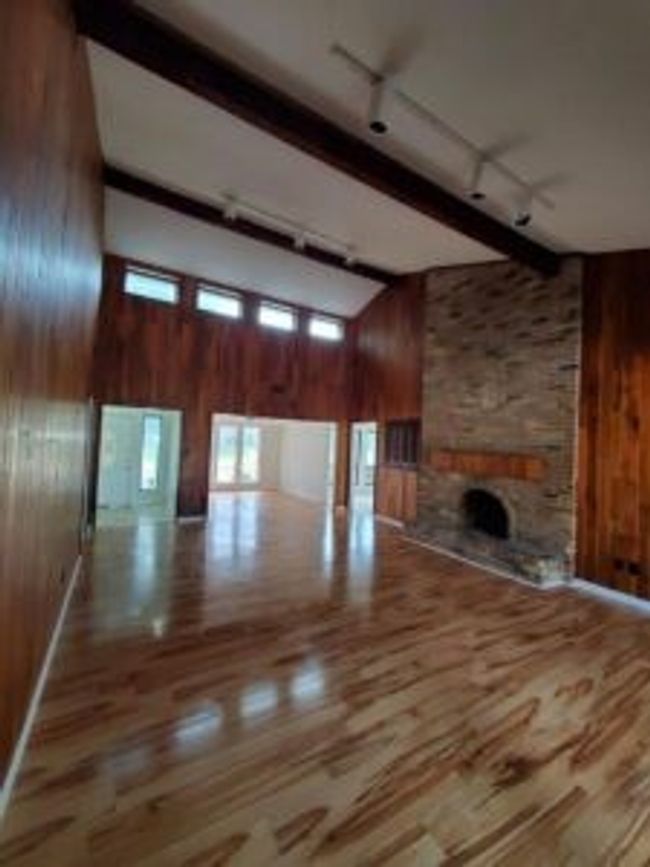 Unfurnished living room featuring wood walls, a high ceiling, track lighting, a fireplace, and wood finished floors | Image 9
