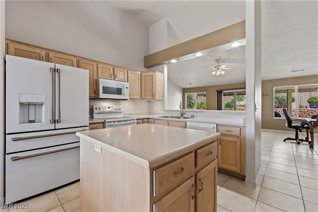 Kitchen featuring white appliances, light brown cabinetry, light tile patterned floors, a kitchen island, and light countertops | Image 15