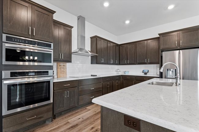 Kitchen with wall chimney exhaust hood, a sink, dark brown cabinets, light stone countertops, and appliances with stainless steel finishes | Image 15