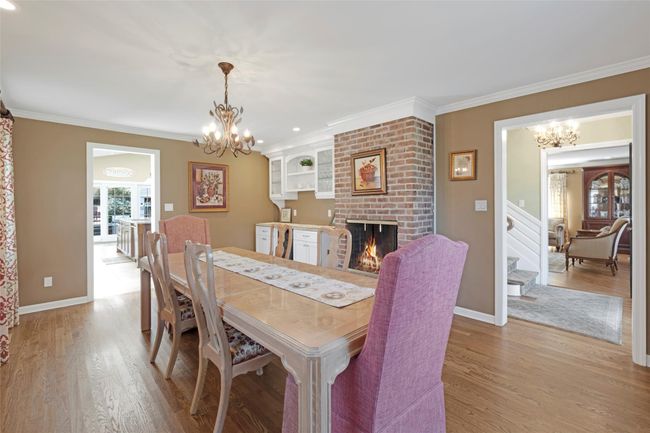 Dining area with light wood-style flooring, a brick fireplace, crown molding, and a chandelier | Image 7