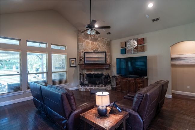 Living room with a ceiling fan, wood finished floors, baseboards, a fireplace, and high vaulted ceiling | Image 6