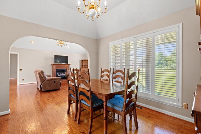 Dining space featuring arched walkways, a chandelier, light wood-style flooring, a fireplace, and vaulted ceiling | Image 6