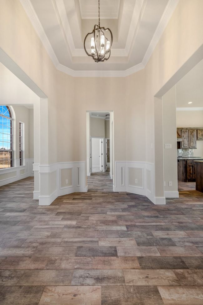 Empty room with a chandelier, a towering ceiling, wood finished floors, ornamental molding, and a raised ceiling | Image 19