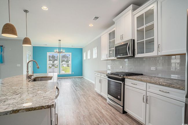 Kitchen featuring stainless steel appliances, white cabinets, decorative backsplash, light wood-style floors, and light stone countertops | Image 8