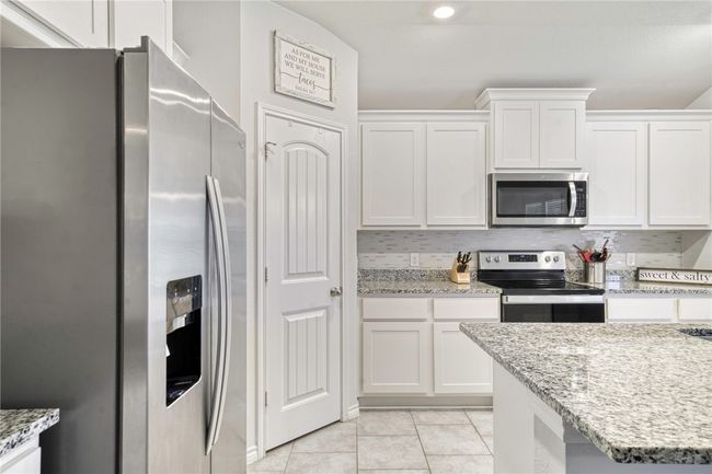 Kitchen with light tile patterned flooring, appliances with stainless steel finishes, white cabinets, backsplash, and light stone countertops | Image 15