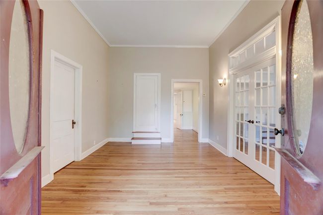 MASSIVE DOUBLE DOORS LEAD TO A GRAND FOYAR SHOWCASING ORIGINAL WOOD FLOORS, WIDE BASE BOARDS, CROWN MOLDING, 11'+ TALL CEILINGS & TRANSOMED FRENCH DOORS WHICH LEAD SEVERAL DIRECTIONS. AHEAD, A HALLWAY LEADS TO ANOTHER FOYAR TO THE BACK ENTRANCE. | Image 5