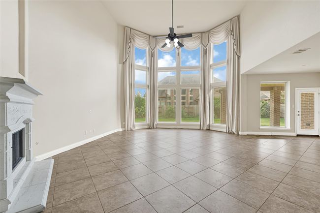 The living room impresses with dramatic high ceilings, a curved wall of towering windows, and a fireplace—all seamlessly connecting to the kitchen and upper-level overlook. | Image 11