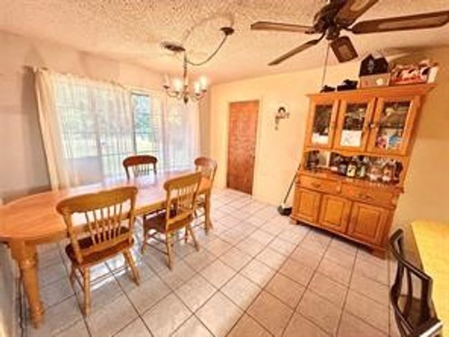 Dining space featuring light tile patterned floors, a textured ceiling, and ceiling fan with notable chandelier | Image 9