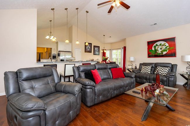 Living area featuring ceiling fan with notable chandelier, visible vents, lofted ceiling, and dark wood-style flooring | Image 4