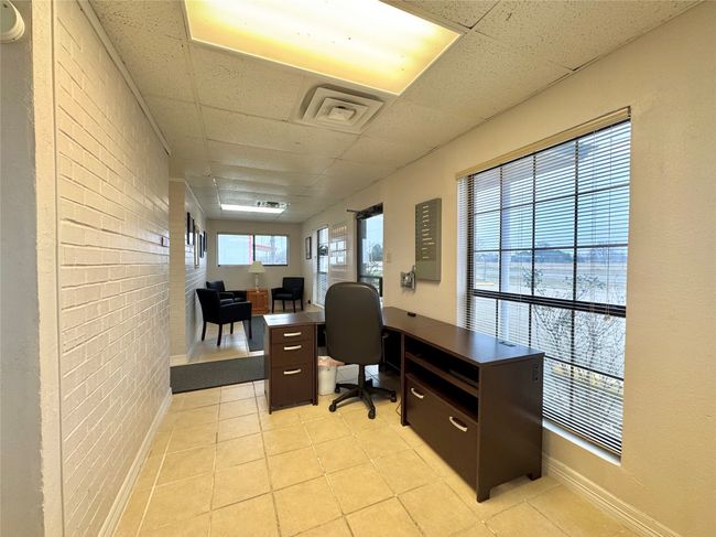 Home office with a paneled ceiling, light tile patterned flooring, and brick wall | Image 32