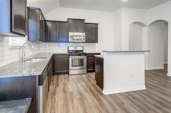 Kitchen with appliances with stainless steel finishes, light wood-style flooring, dark brown cabinets, tasteful backsplash, and light stone countertops | Image 5
