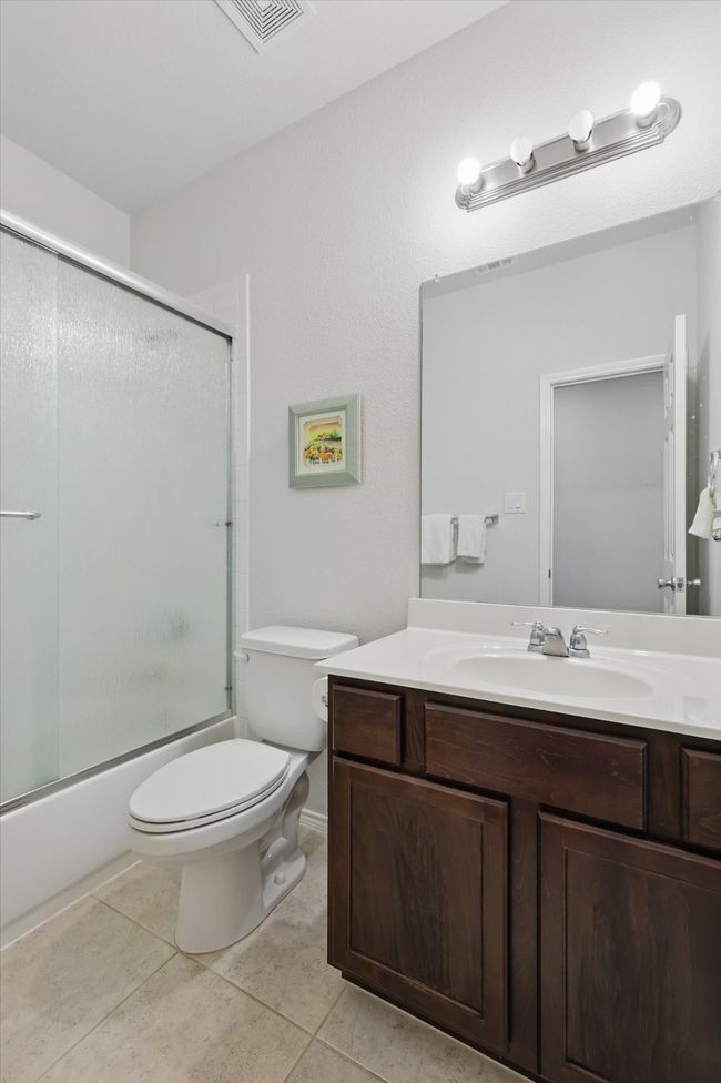 Bathroom featuring tile patterned floors, vanity, bath / shower combo with glass door, toilet, and visible vents | Image 6