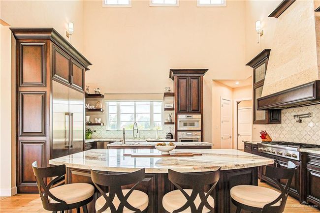 Kitchen with a high ceiling, a breakfast bar, open shelves, maple custom cabinets, and brazilian stone countertops | Image 18