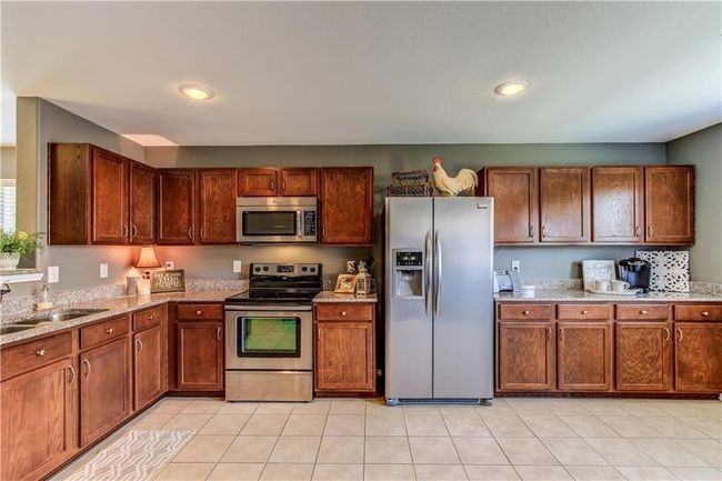 Kitchen featuring stainless steel appliances, light stone countertops, brown cabinets, light tile patterned floors, and recessed lighting | Image 9