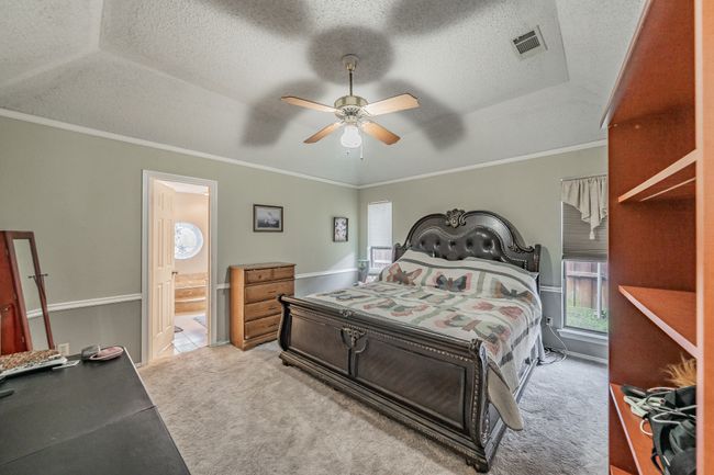 Carpeted bedroom featuring a tray ceiling, a textured ceiling, ensuite bathroom, crown molding, and a ceiling fan | Image 13