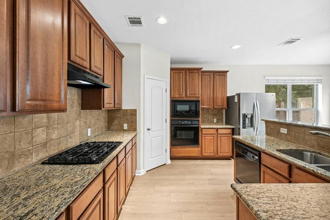 Kitchen with black appliances, under cabinet range hood, light wood-type flooring, brown cabinetry, and stone counters | Image 10