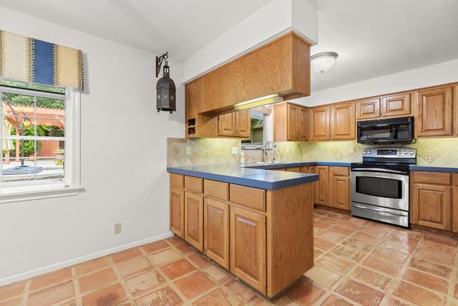 Kitchen with electric range, black microwave, a peninsula, decorative backsplash, and dark countertops | Image 8