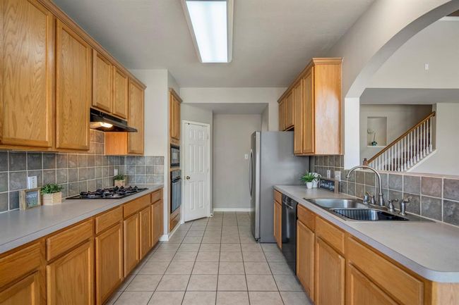 Looking down the length of the kitchen, to the left you’ll find the gas cooktop, built-in oven and microwave, and a convenient corner pantry. On the right, the fridge, dishwasher, and sink are positioned with an opening to the living room, creating an ideal layout for entertaining and daily use. | Image 13