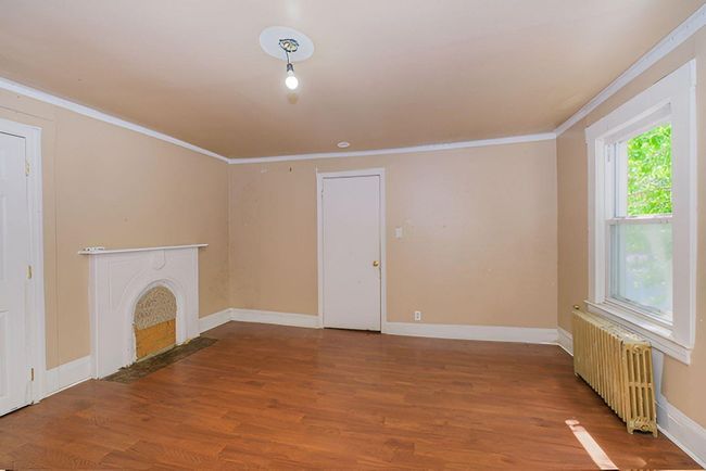 Unfurnished living room with radiator, ornamental molding, wood finished floors, and a fireplace with flush hearth | Image 4