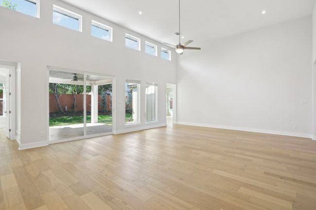 Unfurnished living room with light wood-style flooring, a ceiling fan, a high ceiling, and baseboards | Image 12