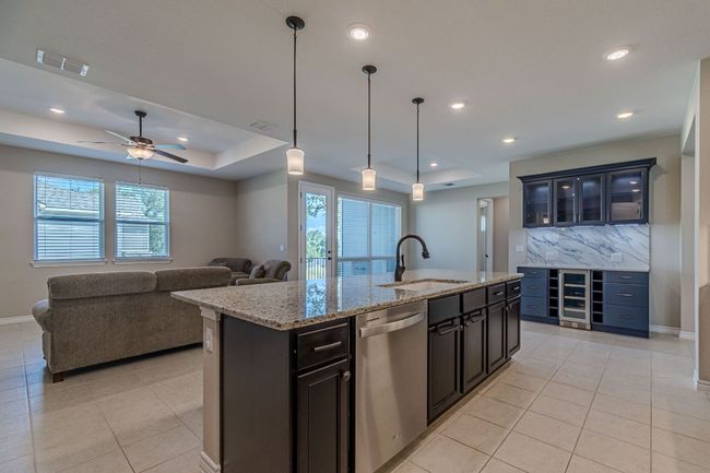 Kitchen featuring a raised ceiling, stainless steel dishwasher, recessed lighting, a center island with sink, and glass insert cabinets | Image 12