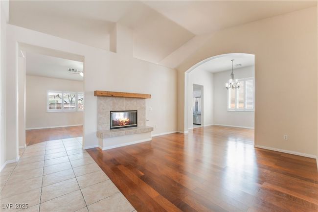 Unfurnished living room featuring a chandelier, light wood-style flooring, arched walkways, a tile fireplace, and baseboards | Image 24