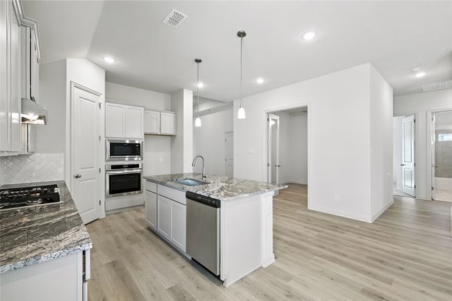 Kitchen with stainless steel appliances, light wood-type flooring, light stone counters, decorative backsplash, and a kitchen island with sink | Image 4