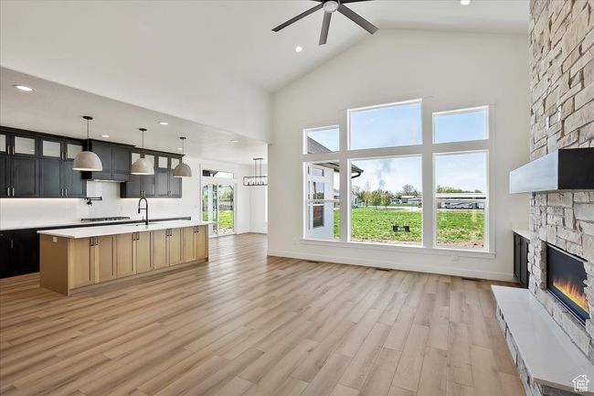 Unfurnished living room featuring a stone fireplace, a ceiling fan, a sink, light wood-style flooring, and high vaulted ceiling | Image 5