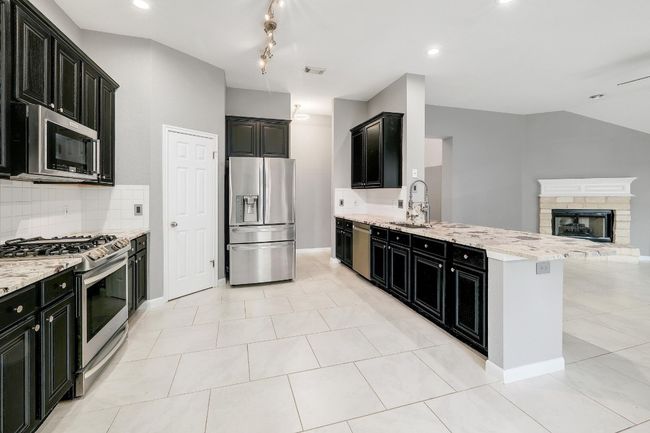 Kitchen featuring a peninsula, a fireplace with raised hearth, stainless steel appliances, dark cabinetry, and open floor plan | Image 11