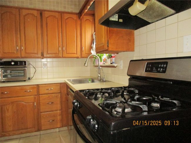 Kitchen with gas range, under cabinet range hood, brown cabinets, and a sink | Image 8