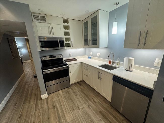 Kitchen with appliances with stainless steel finishes, a sink, dark wood-style flooring, white cabinetry, and open shelves | Image 4