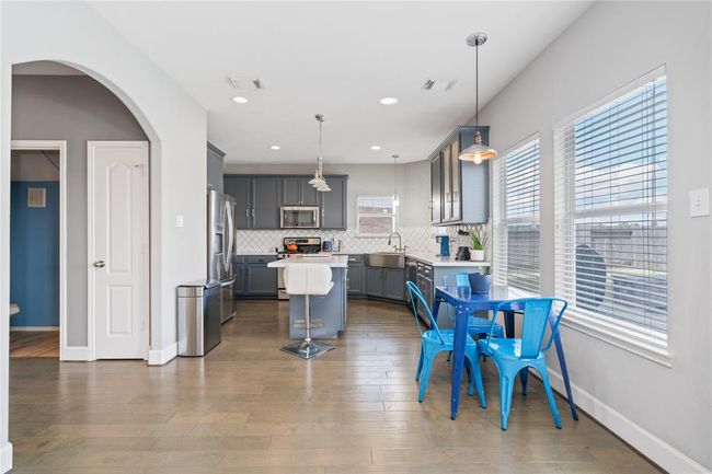 This photo showcases a modern kitchen with gray cabinetry, stainless steel appliances, and a central island with bar seating. It features a cozy breakfast nook with bright blue chairs next to large windows, allowing plenty of natural light. The space has an open and inviting layout, ideal for family gatherings. | Image 19