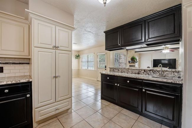 This is a spacious kitchen featuring contrasting dark wood cabinetry with light countertops, modern appliances, tiled flooring, and ample natural light from the windows. The room flows into an adjacent living area, providing an open concept feel. | Image 14