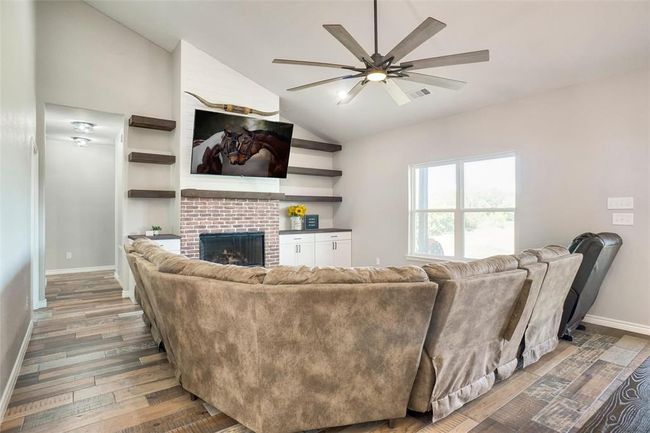 Living room with lofted ceiling, a fireplace, wood-type flooring, and ceiling fan | Image 4