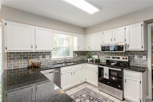 Kitchen with white cabinets, stainless steel appliances, dark stone countertops, a sink, and tasteful backsplash | Image 6
