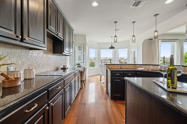 Kitchen with dark stone countertops, decorative light fixtures, dark brown cabinets, dark wood-style floors, and arched walkways | Image 20