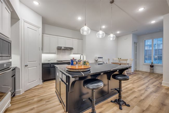 Kitchen with under cabinet range hood, light wood-style floors, a kitchen bar, decorative backsplash, and stainless steel appliances | Image 10